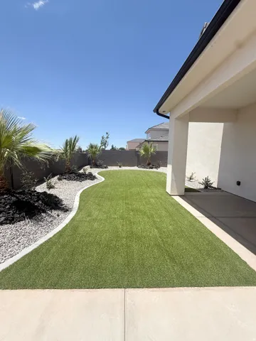Expansive backyard featuring artificial turf, decorative rock landscaping, mature desert plantings, and a concrete patio