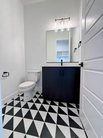 Bathroom featuring a geometric black and white tile floor, a dark wood-finish vanity with a light-colored countertop, and a contemporary three-light vanity fixture