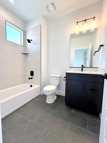 Modern bathroom featuring dark gray floor tiling, a white tub with matte black fixtures, and a sleek black vanity with a white countertop