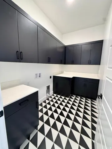 Laundry room featuring a geometric black and white floor tile pattern, extensive dark cabinetry, light-toned countertops, and bright white walls