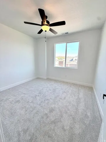 Spacious room featuring light gray carpeting, crisp white walls, a large window, a ceiling fan with integrated lighting, and white baseboards