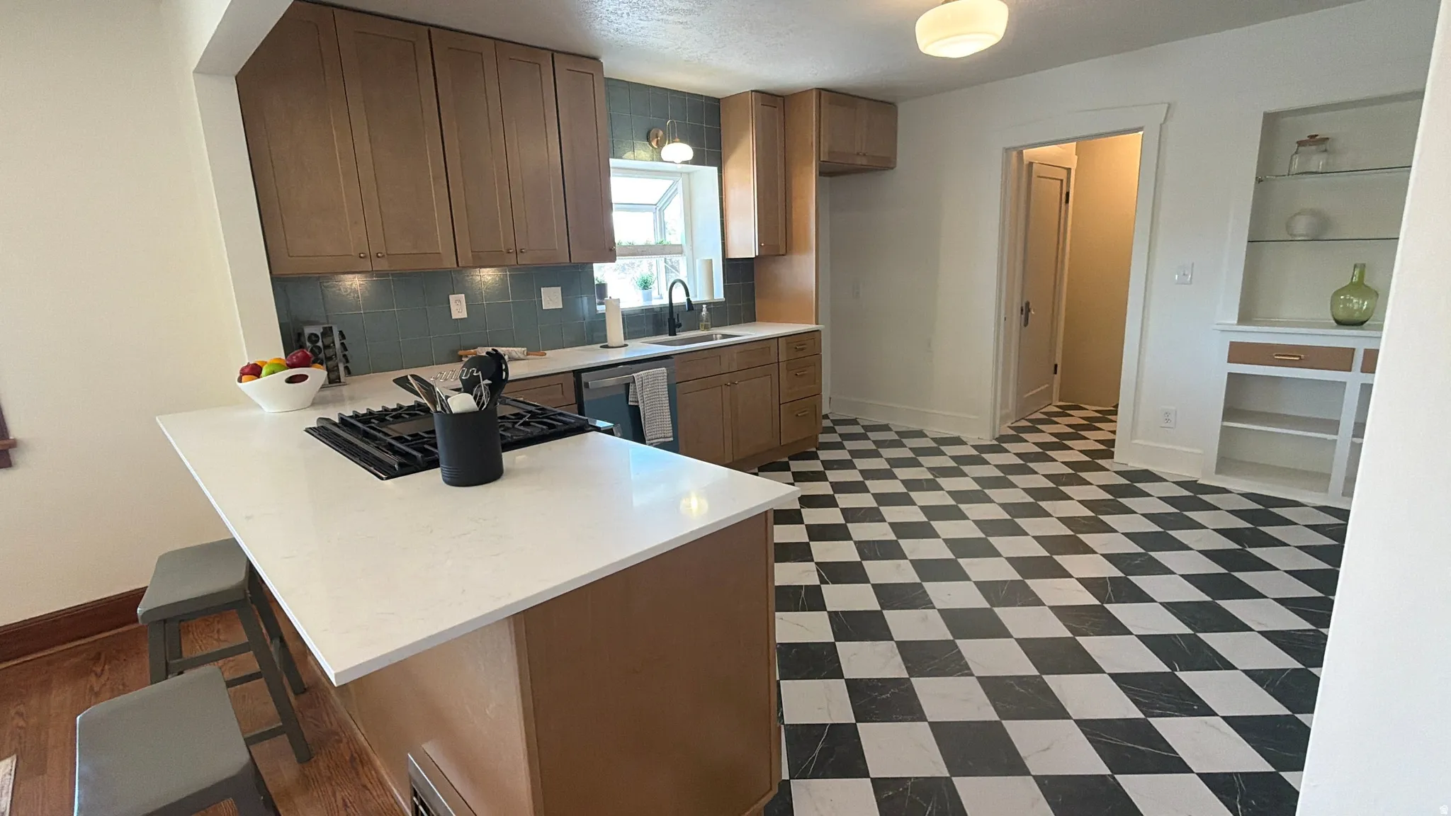 Kitchen featuring a checkerboard floor, recessed lighting, light wood-finish cabinetry, a white countertop island with a built-in cooktop, and a blue tile backsplash