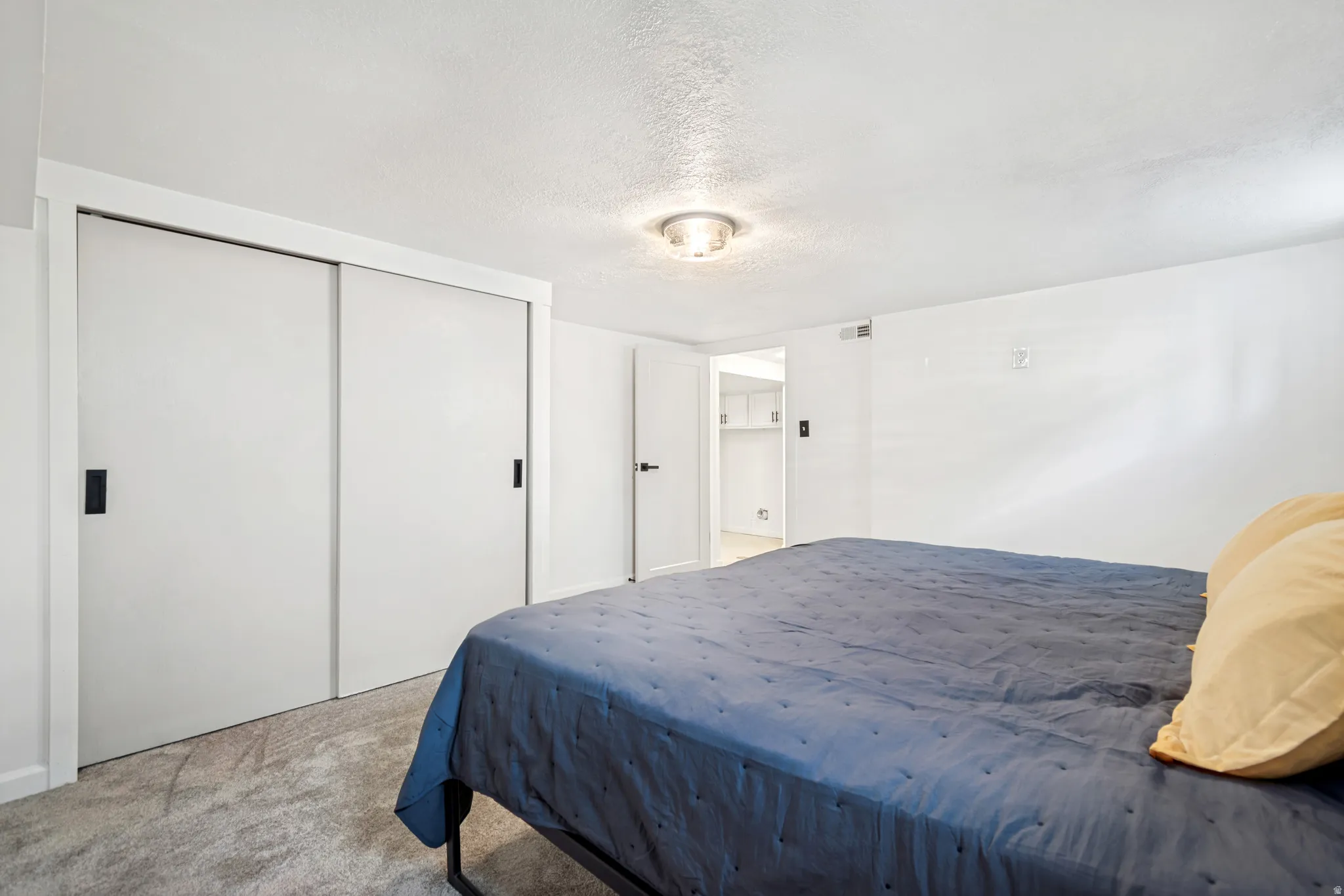 Bedroom 2. White sliding closet doors with matte black hardware, textured ceiling, recessed ceiling light fixture, and plush carpet flooring