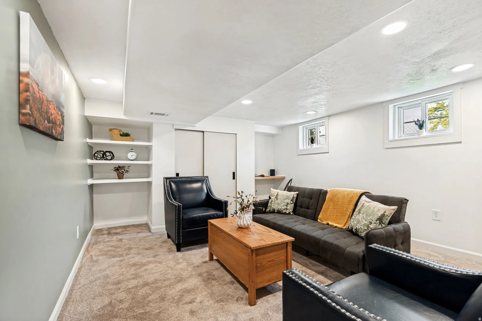 Recessed lighting illuminates this versatile living space, featuring neutral carpeting and built-in shelving