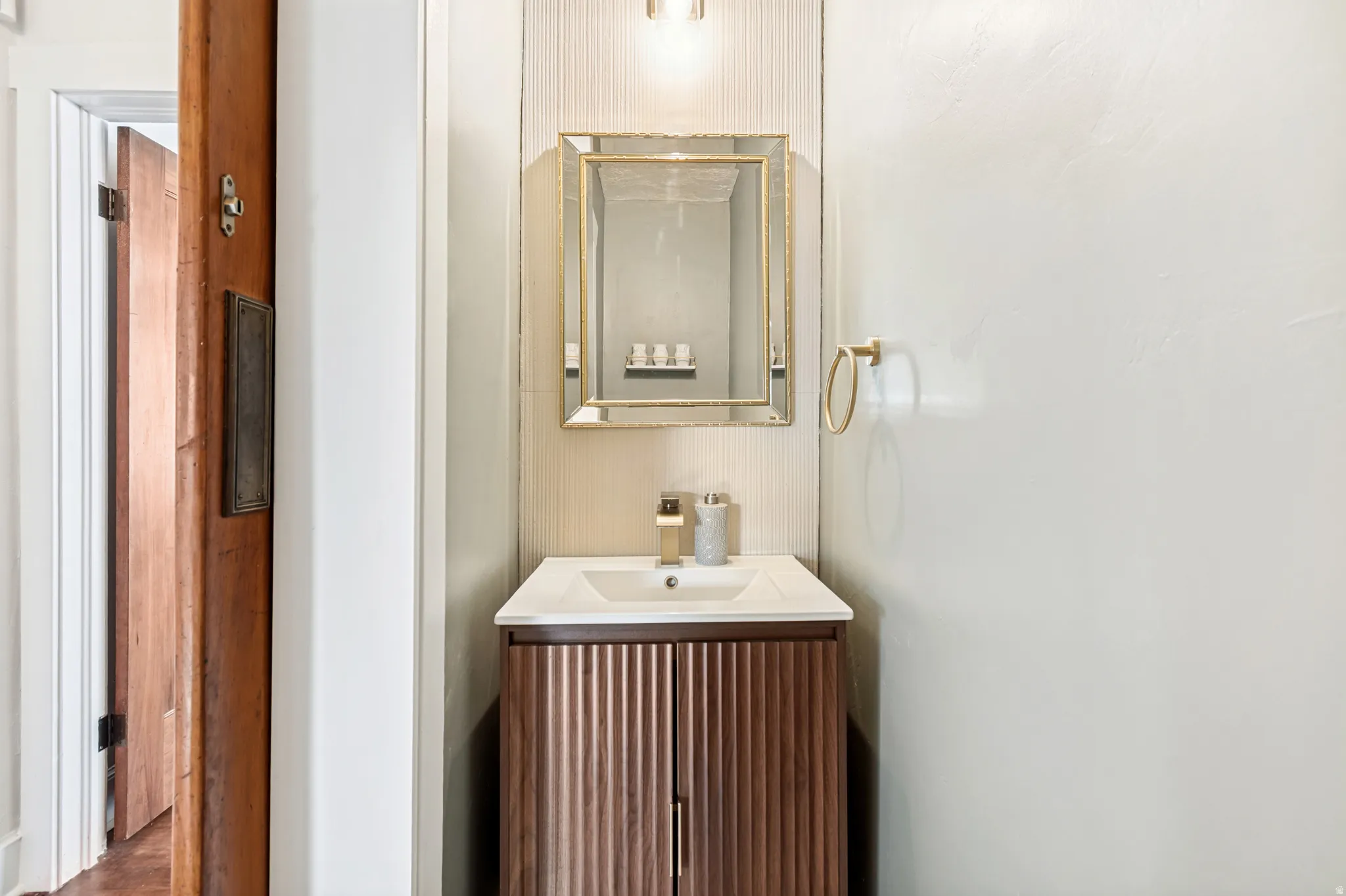 Half Bath. Modern vanity with a fluted wood-finish cabinet, integrated white sink, and gold-toned faucet