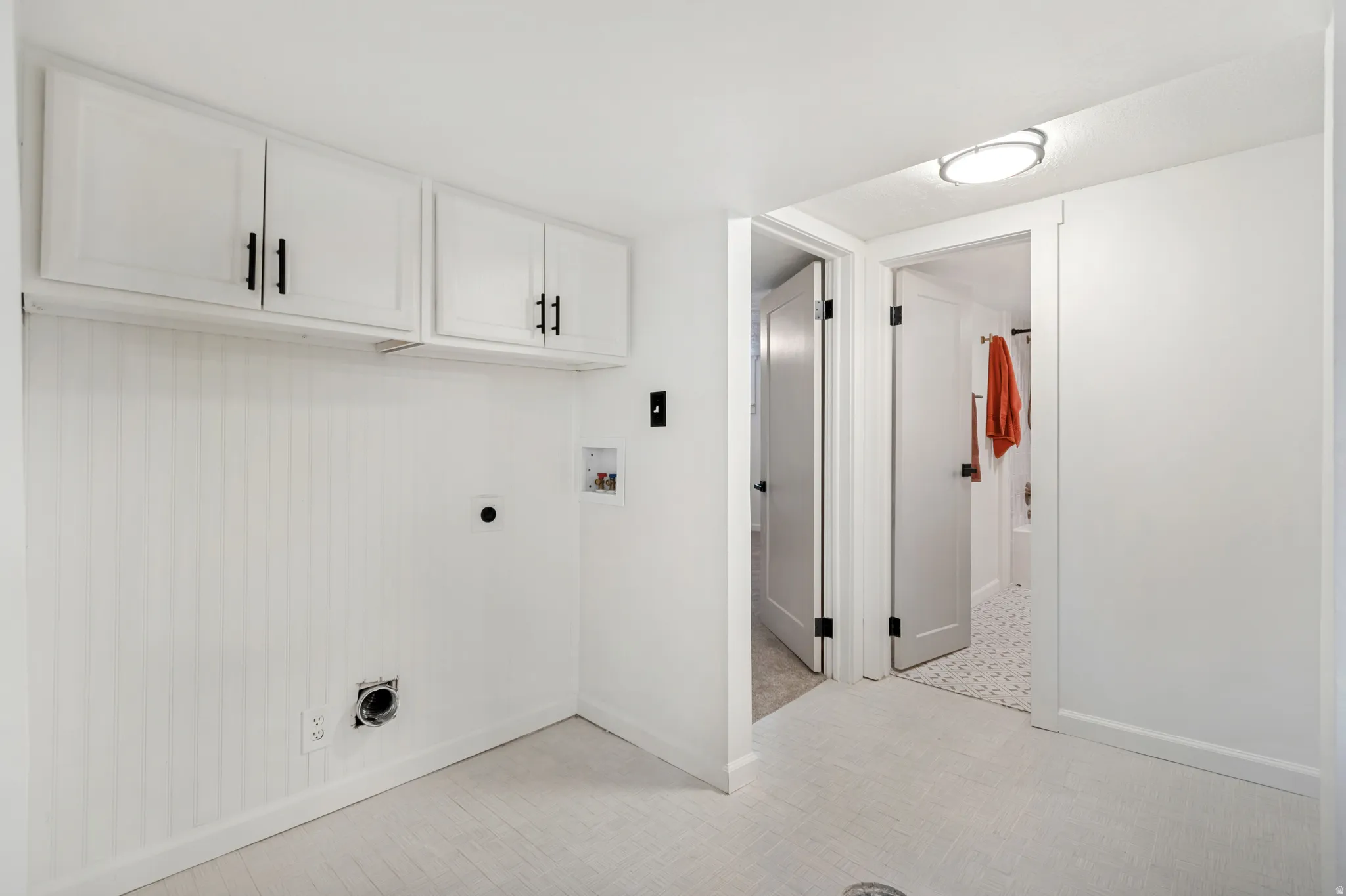 Dedicated utility area featuring white cabinetry with black hardware, beadboard wall paneling, and light-toned flooring