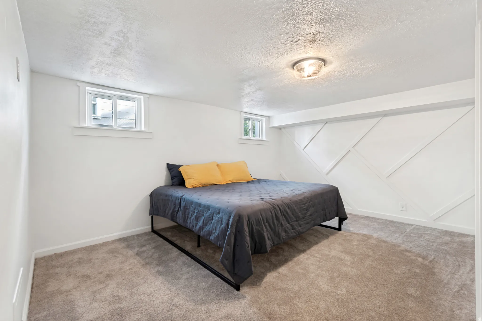 Bedroom 2. Carpeted room featuring a decorative accent wall with geometric paneling, two windows, and a flush-mount ceiling light fixture