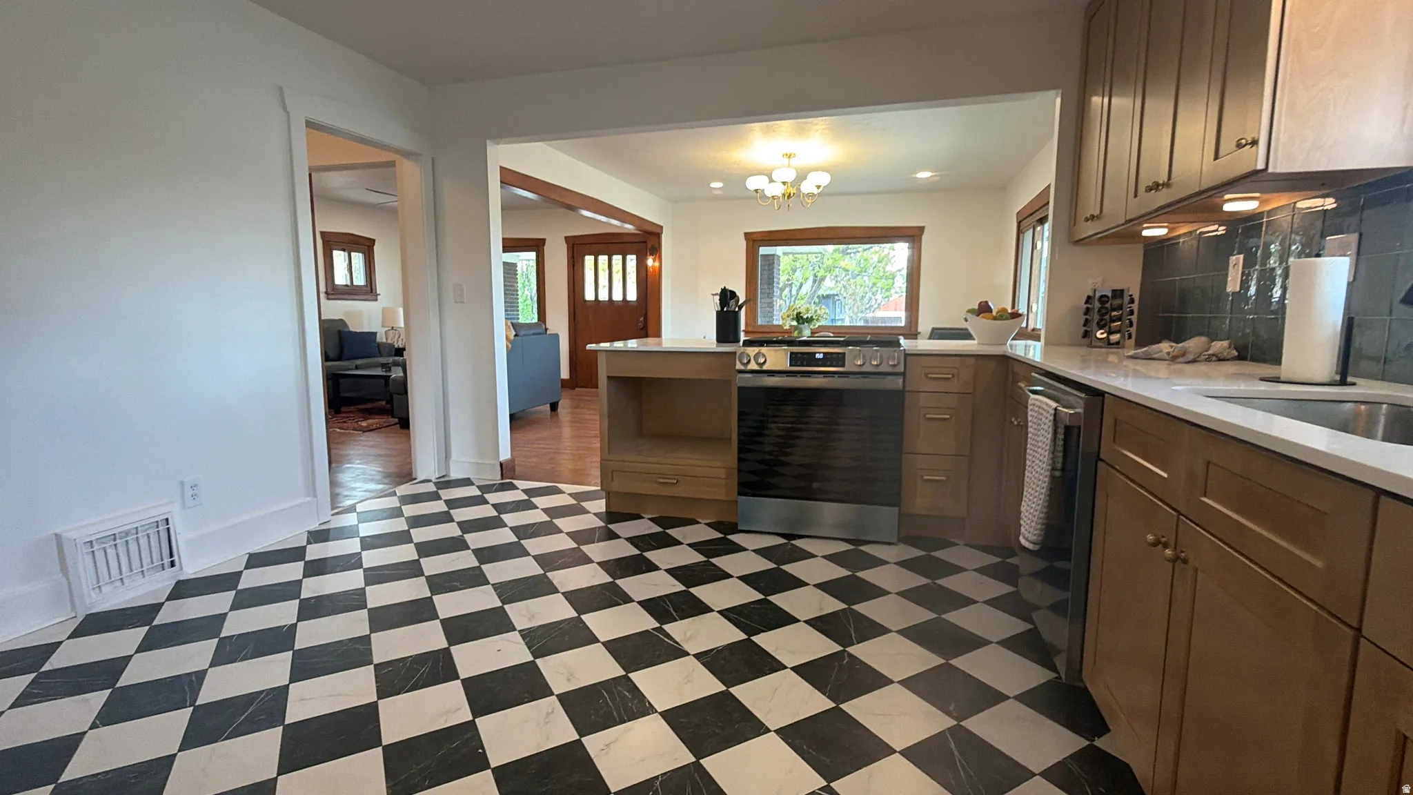 Kitchen featuring checkerboard flooring, natural wood-finish cabinetry, stainless steel range, integrated dishwasher, and a stainless steel sink with a light-toned countertop