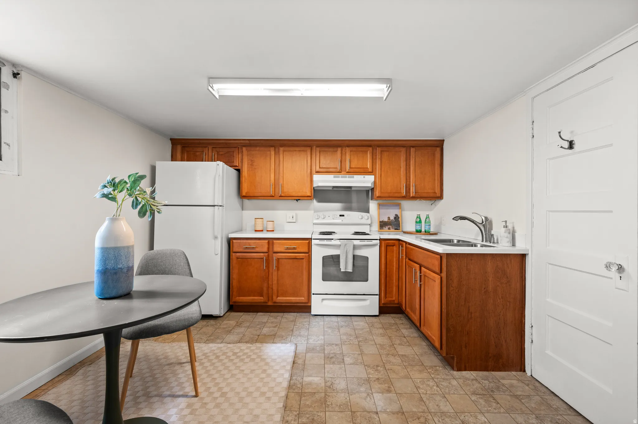 Functional kitchen featuring wood cabinetry, white countertops, a stainless steel sink, and white appliances
