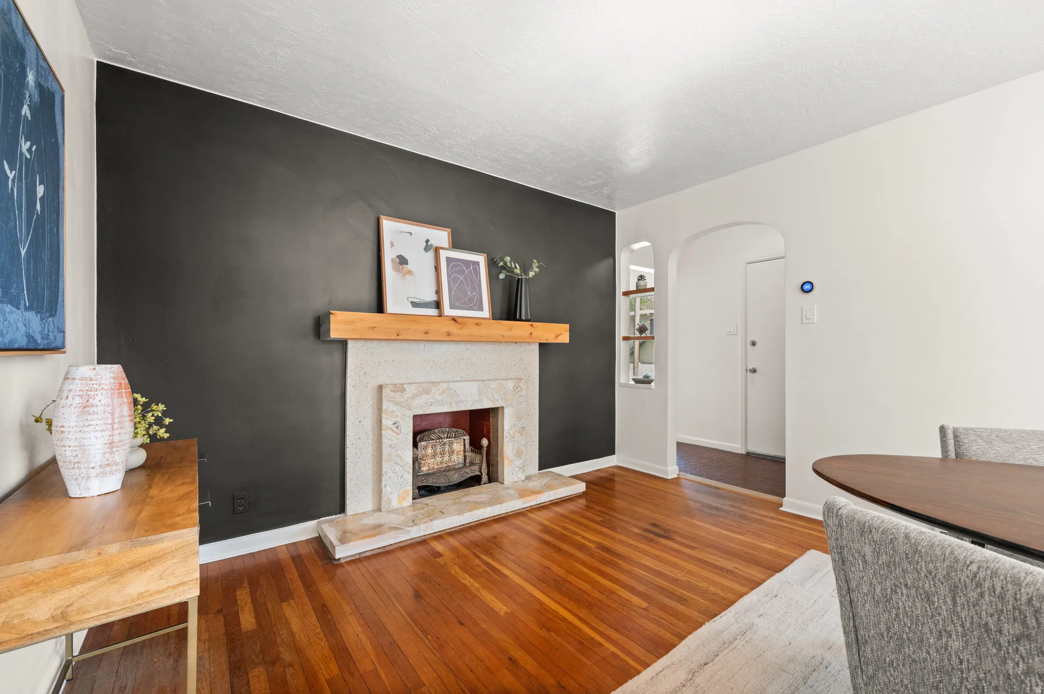 Living area featuring wood-finish flooring, a stone fireplace with a wood mantle, and a built-in arched display niche