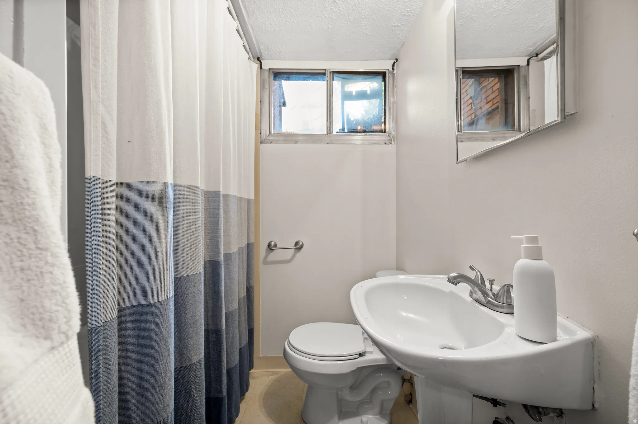 Compact bathroom featuring a wall-mounted pedestal sink with a chrome faucet, a toilet, a small window, and a wall-mounted medicine cabinet with a mirror
