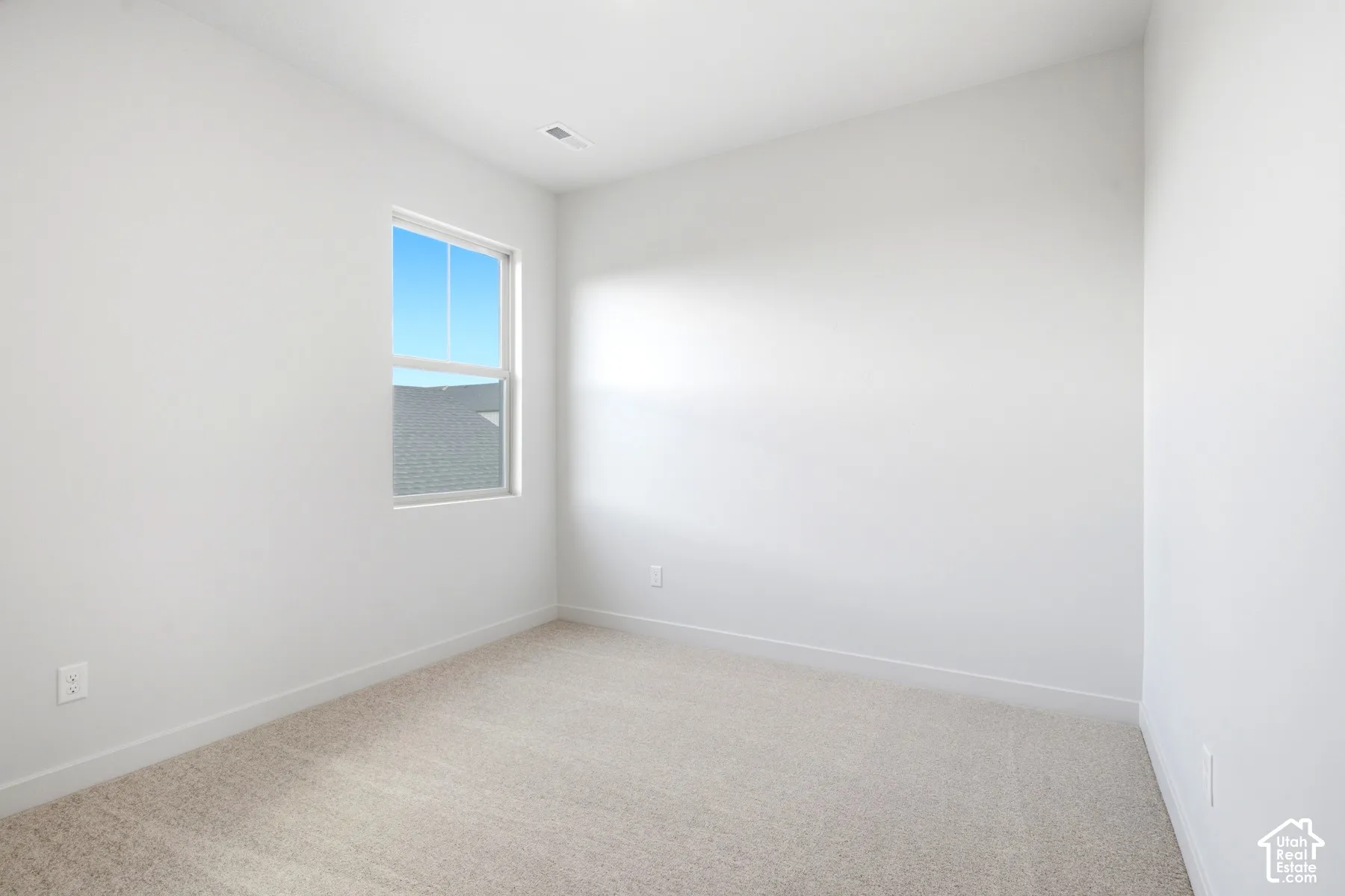 Bright room with neutral wall paint, light-colored carpet flooring, white baseboards, and a double-hung window