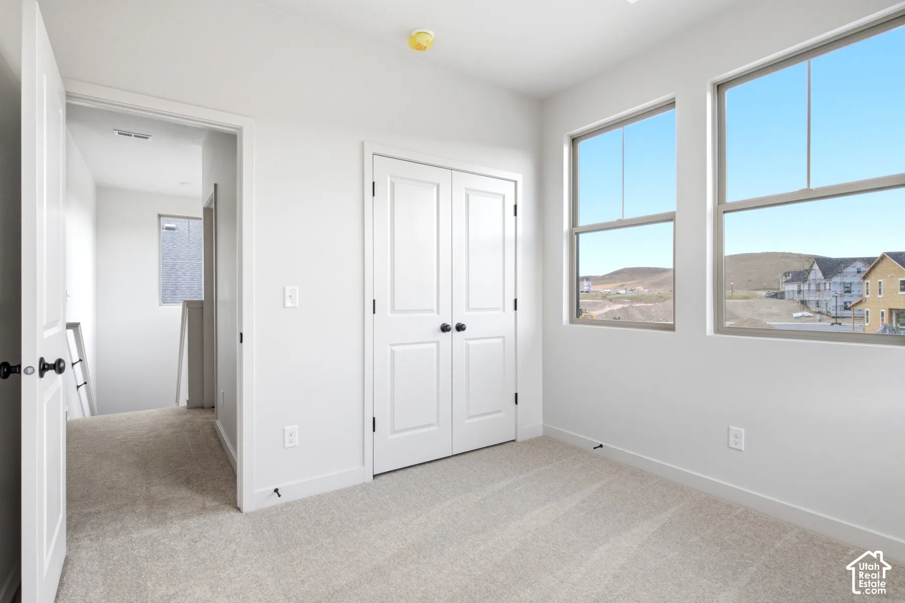 Bright room featuring two large windows, white walls, and light-colored carpet flooring