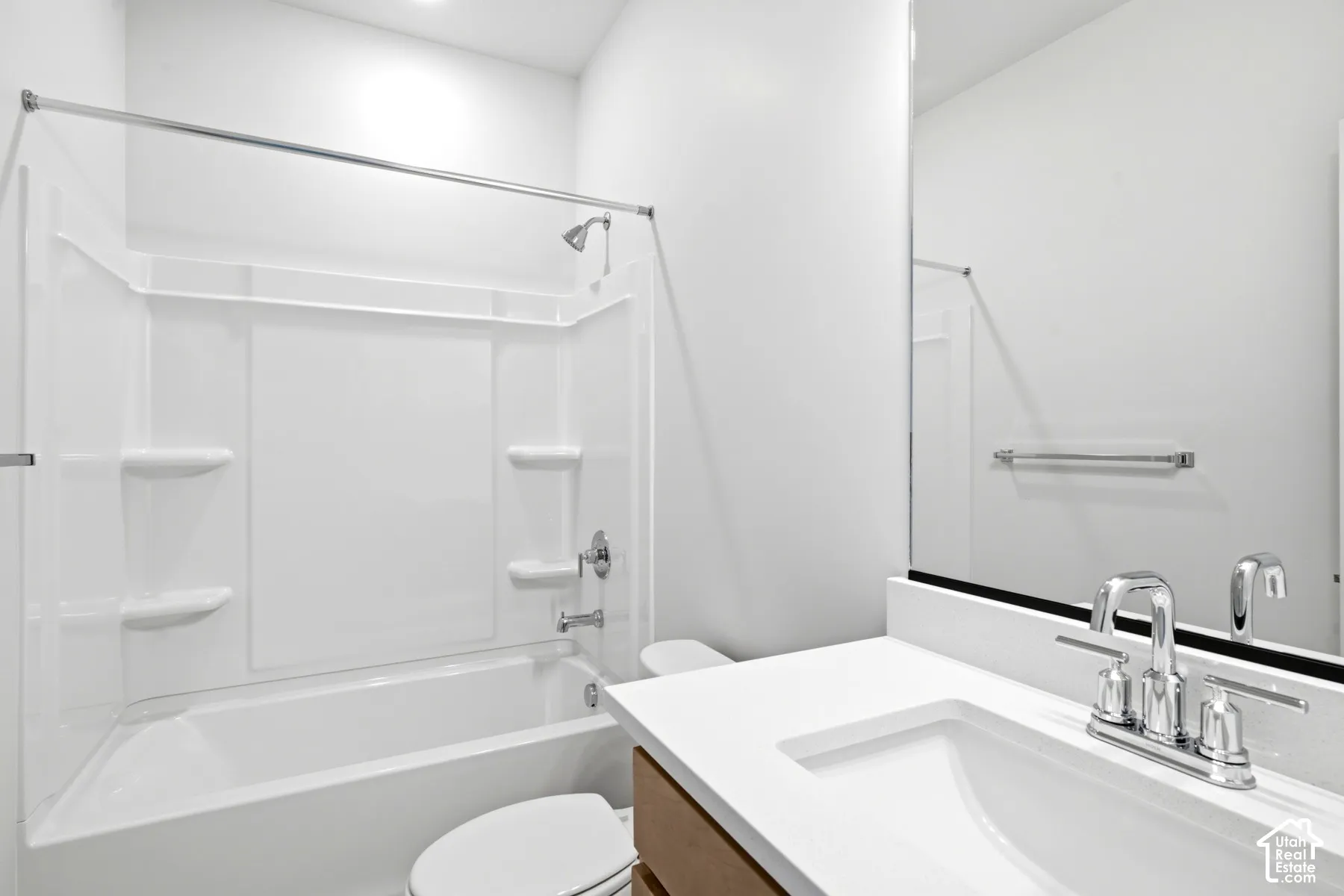 Bathroom featuring a shower-tub combination with integrated shelving, a white toilet, and a vanity with a white countertop and a chrome faucet