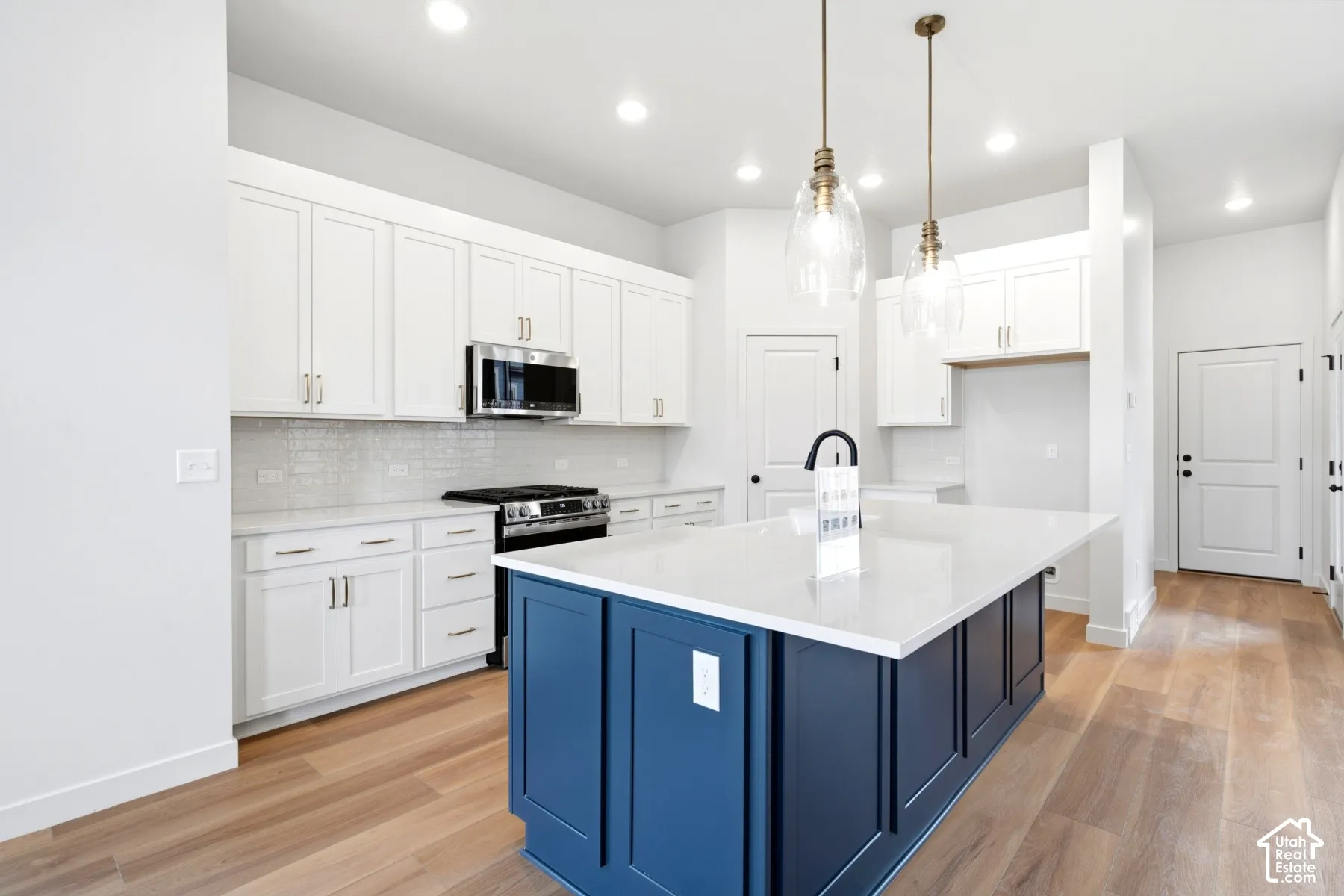 Kitchen featuring a deep blue island with a white countertop, white shaker cabinetry, stainless steel appliances, and light wood-finish flooring