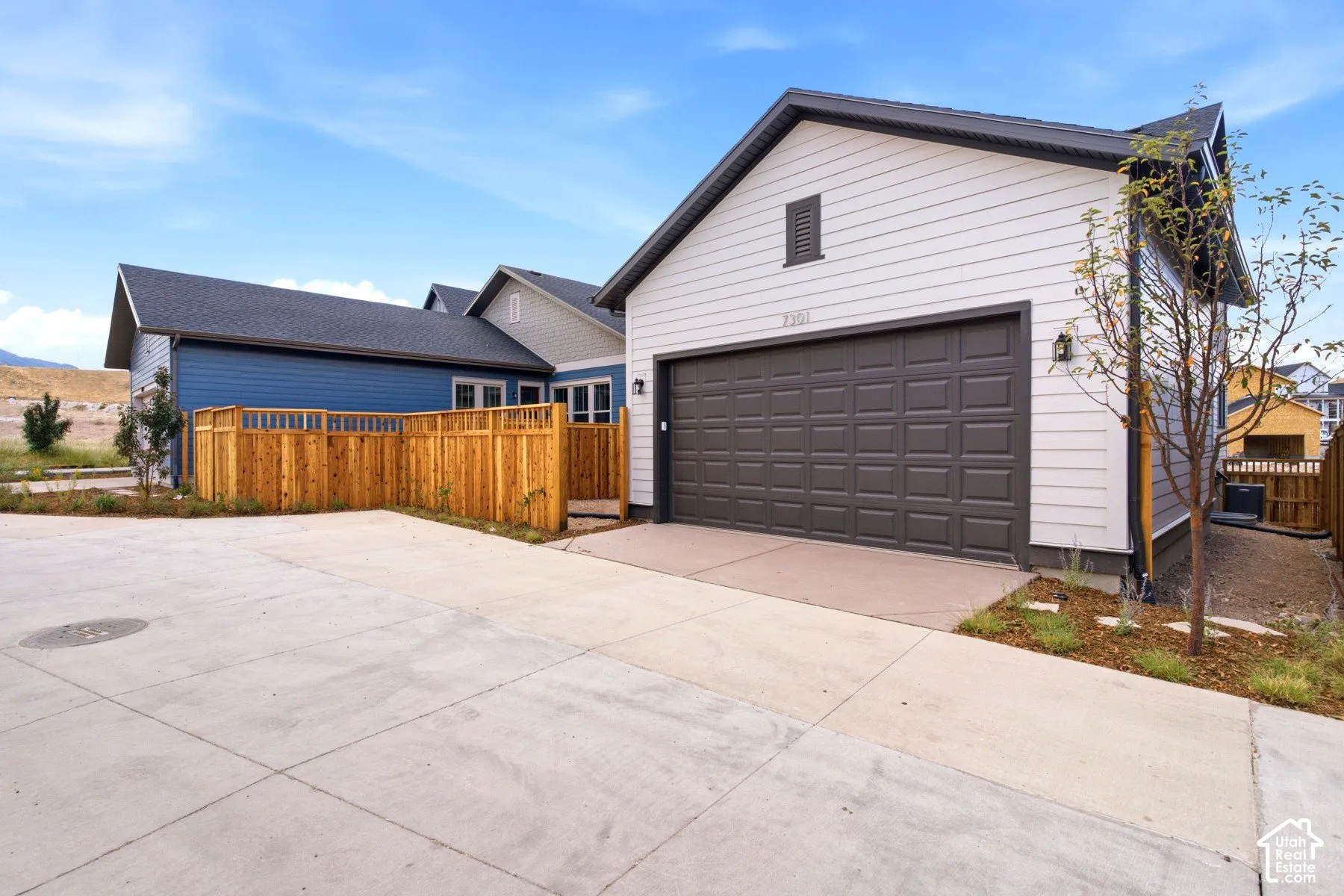 Attached garage with a dark paneled door and light siding, featuring black trim and exterior lighting