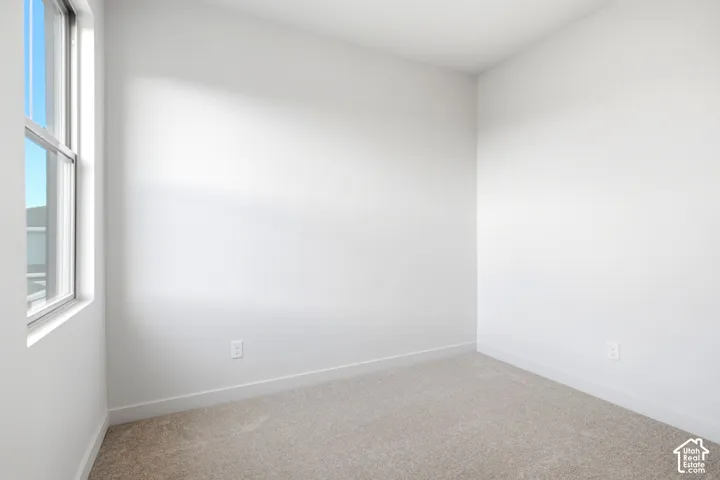 Bright interior space featuring a window, light beige carpet, white walls, and white baseboards