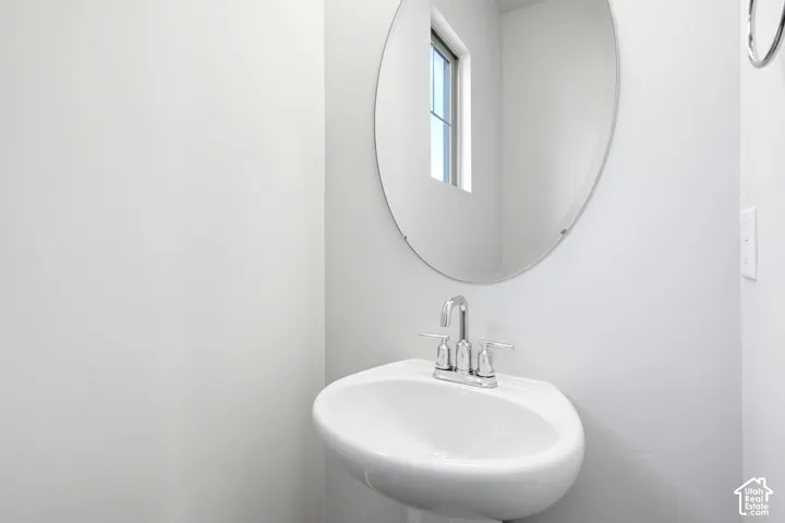 Pedestal sink with chrome faucet, complemented by an oval mirror and natural light from a window