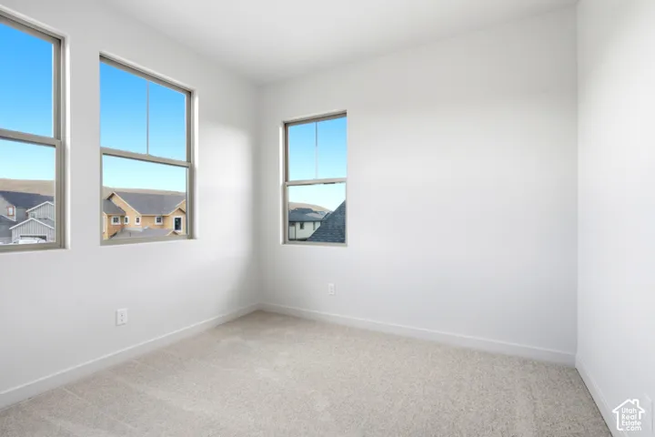Bright interior space featuring three large windows, light gray carpeting, crisp white walls, and white baseboards