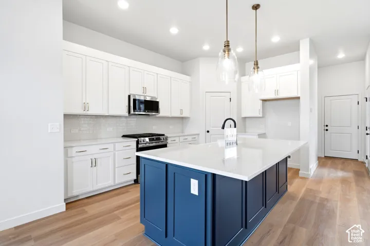 Kitchen featuring a deep blue island with a white countertop, white shaker cabinetry, stainless steel appliances, and light wood-finish flooring