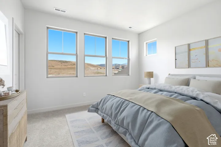 Bright bedroom featuring three large windows, an additional small window, light gray carpet, and white painted walls