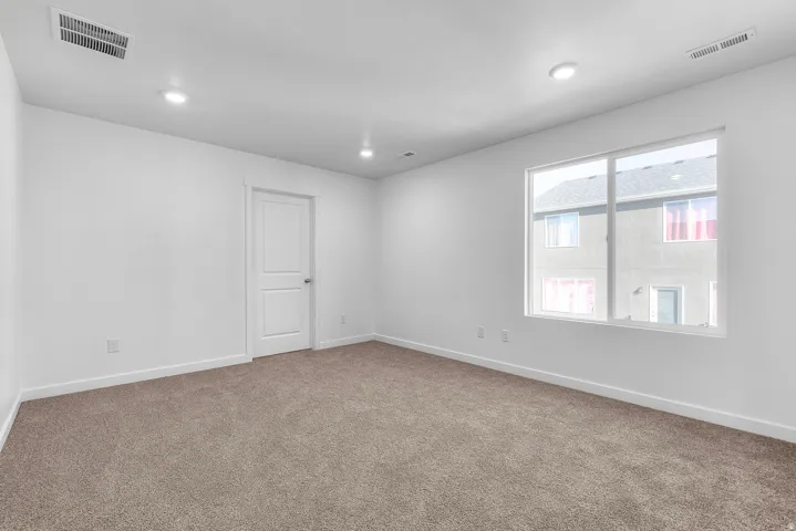 Spacious room featuring neutral carpeting, white walls, recessed lighting, and a large window