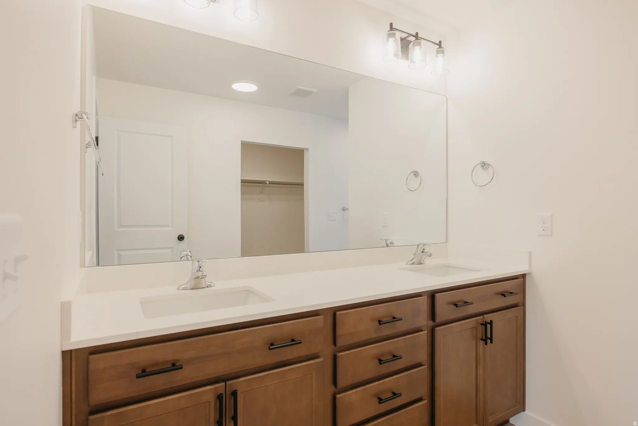 Dual sink vanity with wood-finish cabinetry, quartz-style countertop, and contemporary hardware