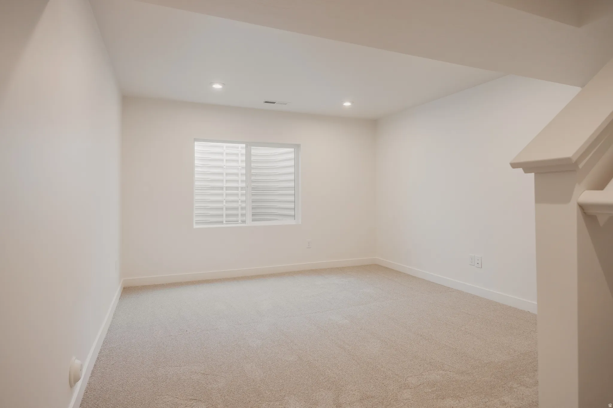 Spacious room with plush carpeting, recessed lighting, and a white egress window