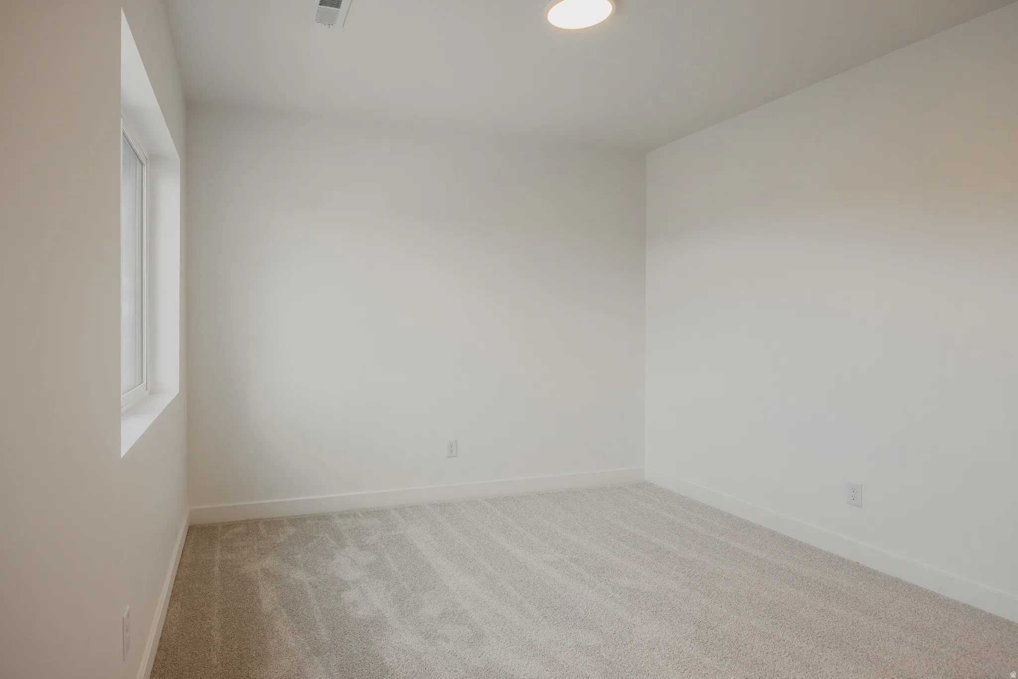 Light-filled room featuring a rectangular window, plush carpet flooring, white baseboards, a flush-mount ceiling light, and neutral wall tones