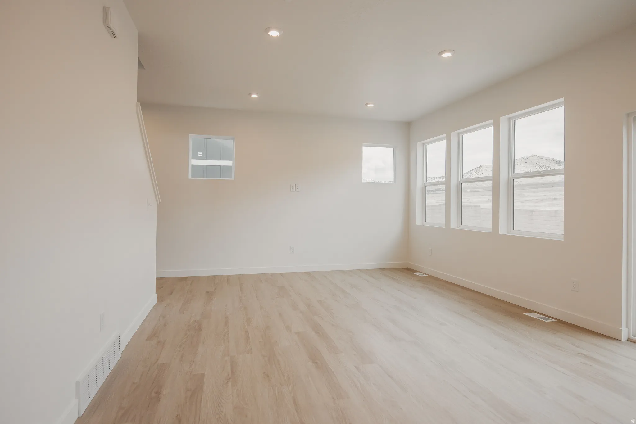 Spacious room featuring light wood-finish flooring, recessed lighting, multiple windows providing natural light, and a mountain backdrop