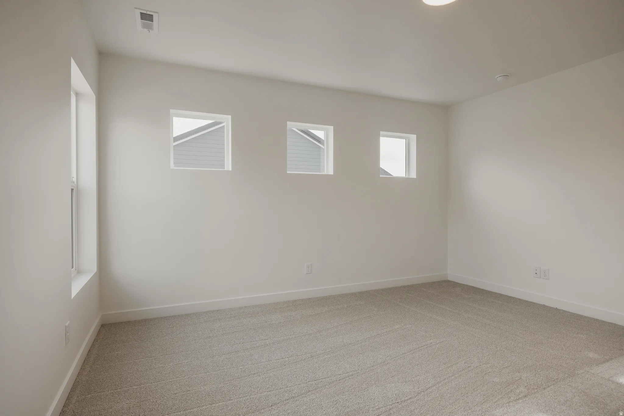 Spacious room featuring neutral carpeting, white baseboards, and bright white walls