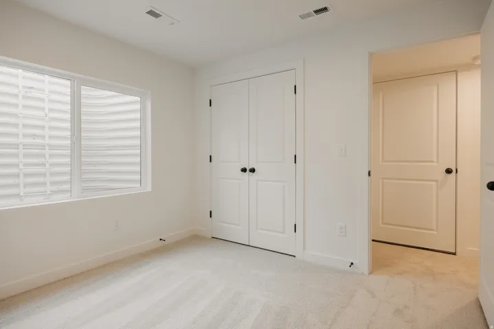 Bedroom featuring light-toned carpet, a window with a window well, white baseboards, and white two-panel doors with black hardware