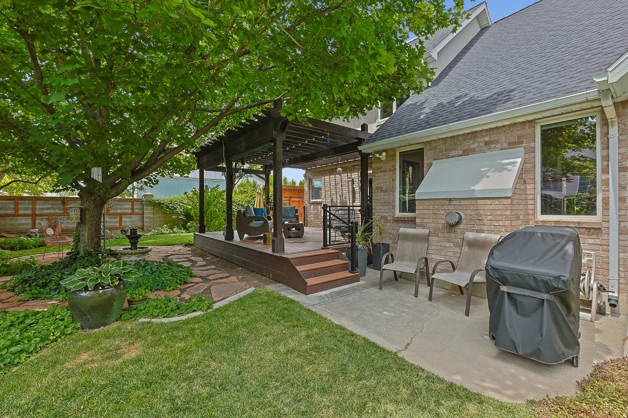 Backyard featuring Brick exterior featuring multiple large windows, a concrete patio, and a well-maintained lawn with mature landscaping