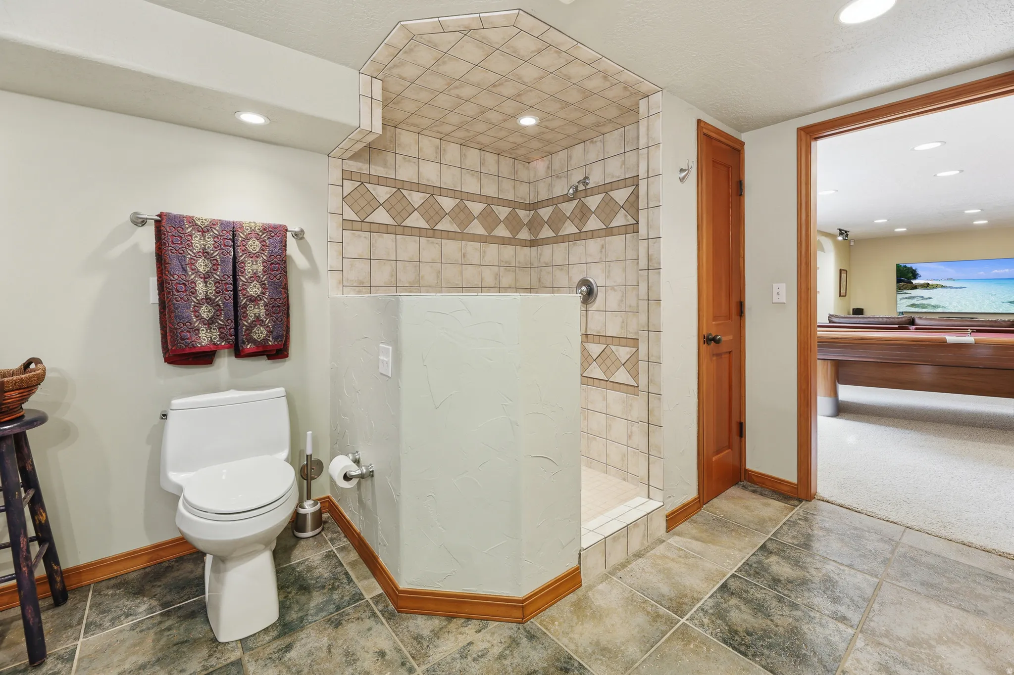 Spacious bathroom featuring an open tiled shower with a built-in bench, a glass block window, a pedestal sink, recessed lighting, and large format stone-look floor tiles