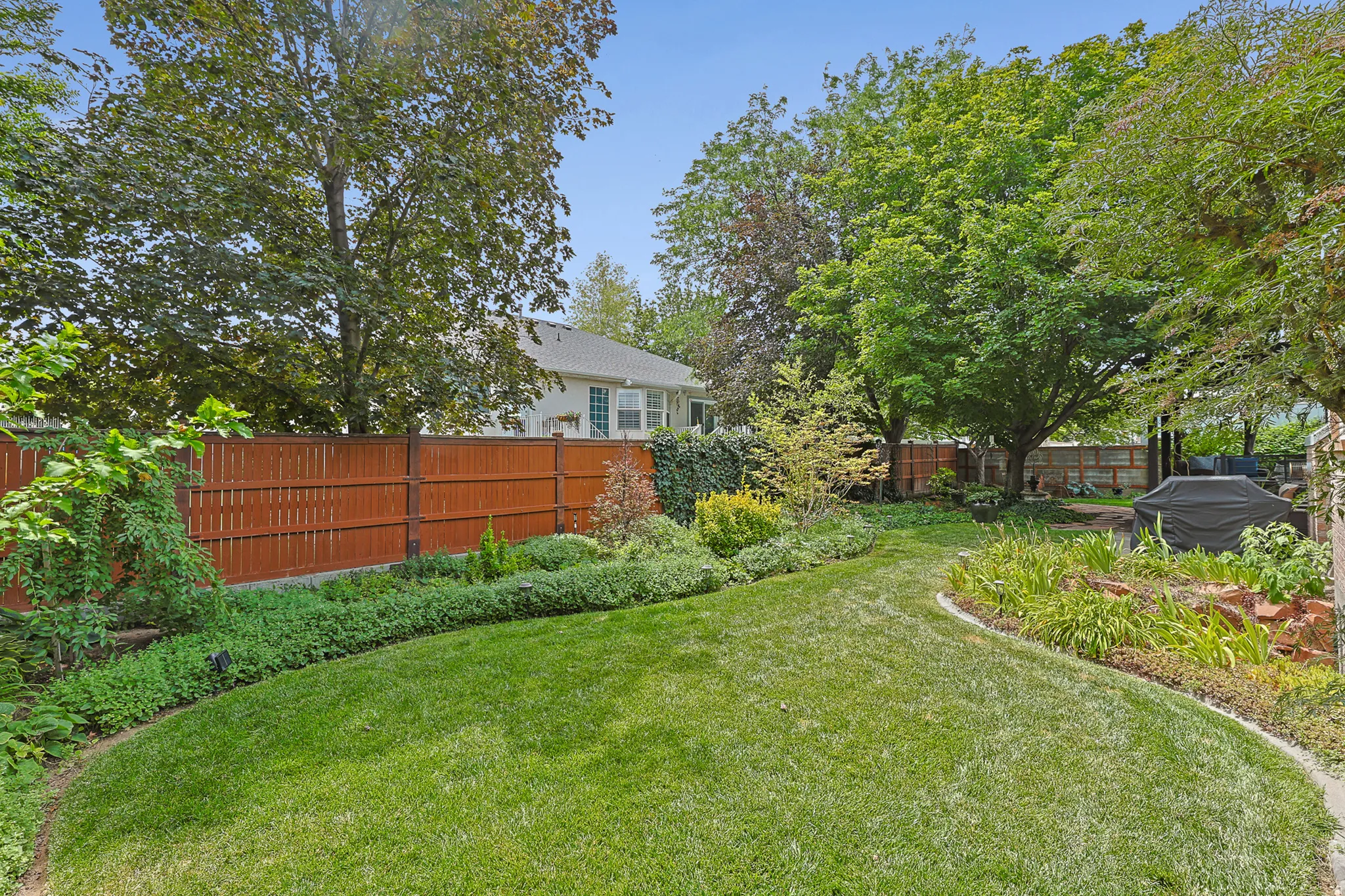 Expansive backyard featuring a manicured lawn, established landscaping borders, a privacy fence, and mature trees