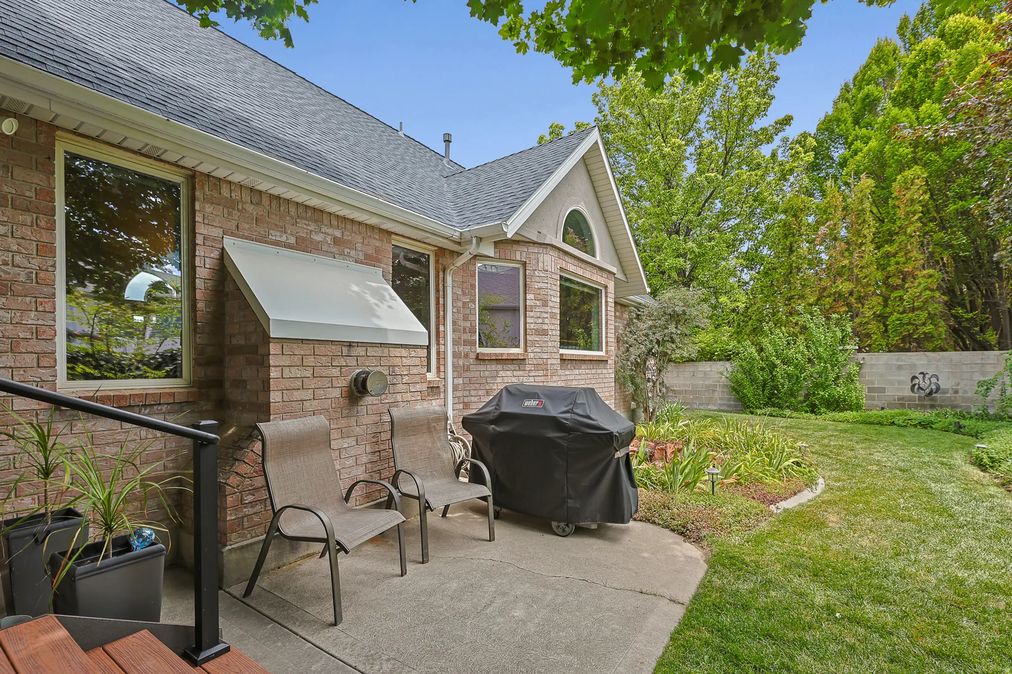 Brick exterior featuring multiple large windows, a concrete patio, and a well-maintained lawn with mature landscaping