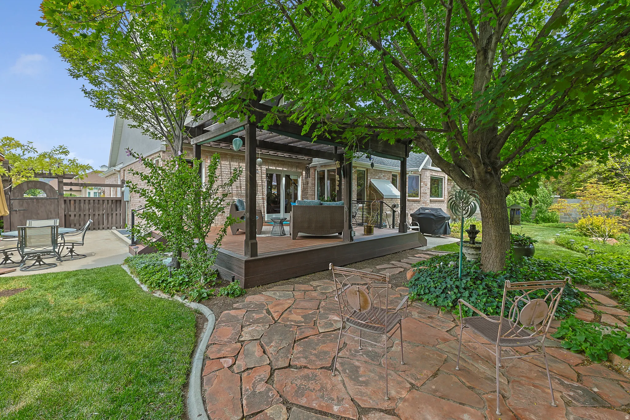 Expansive landscaped backyard featuring a flagstone patio, a raised wood-finish deck with a pergola, a manicured lawn, and mature trees
