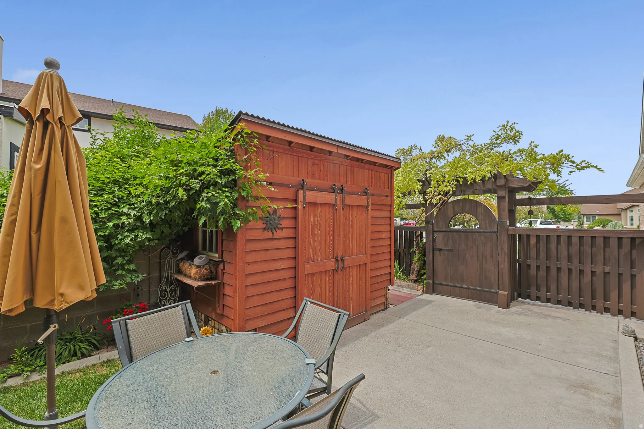 Another private outdoor patio featuring a concrete surface, a beautiful wood garden shed with barn doors, and a decorative wood-finish gate