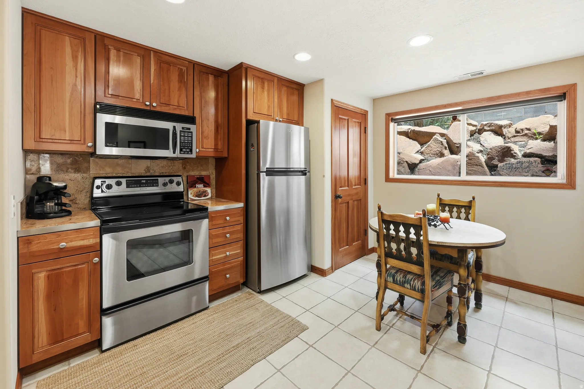 Kitchen featuring wood cabinetry, stainless steel appliances, tile flooring, stone backsplash, and recessed lighting