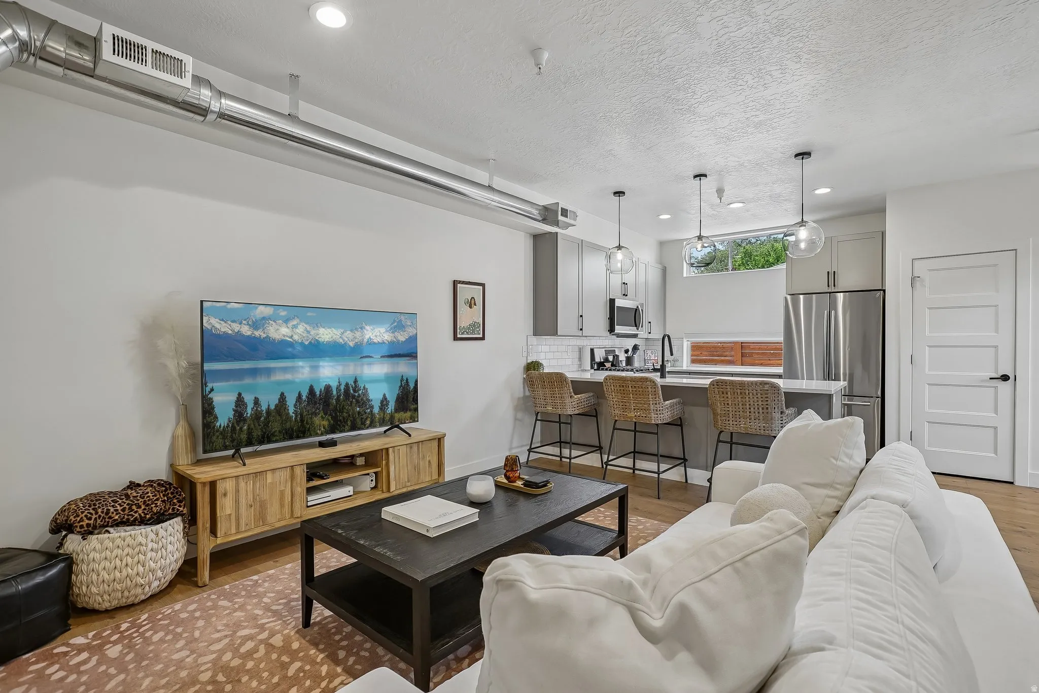 Open-concept living space featuring wood-finish flooring, recessed lighting, and exposed ductwork