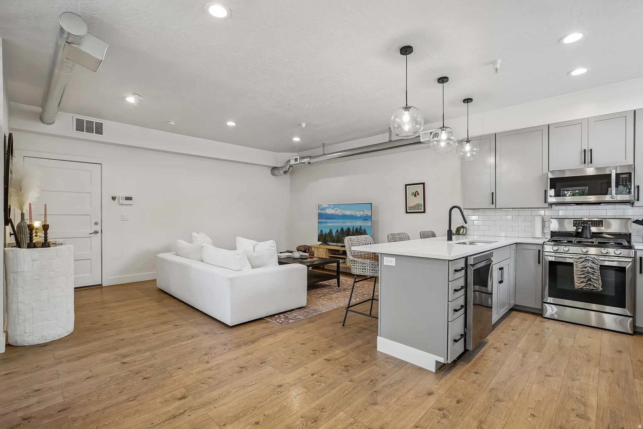 Open-concept living space featuring wood-finish flooring, recessed lighting, and exposed ductwork