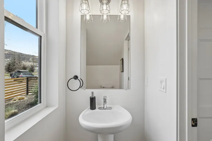 Pedestal sink featuring a chrome faucet, black towel ring, and overhead industrial-style vanity lighting