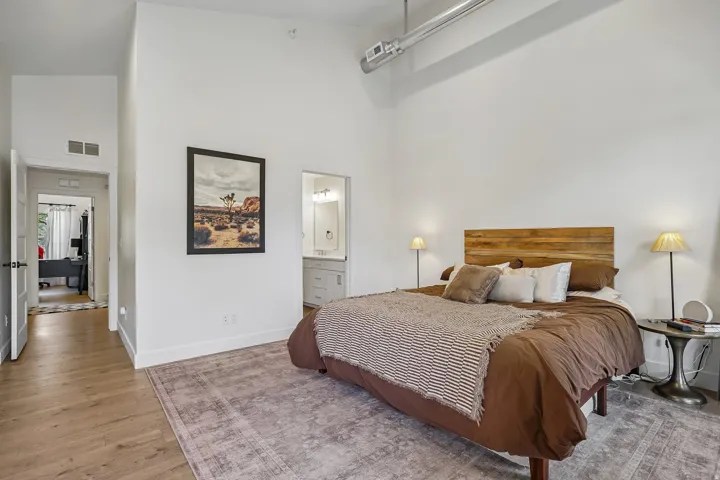 Spacious room featuring high ceilings, exposed ductwork, wood-finish flooring, and a private ensuite bathroom with a vanity