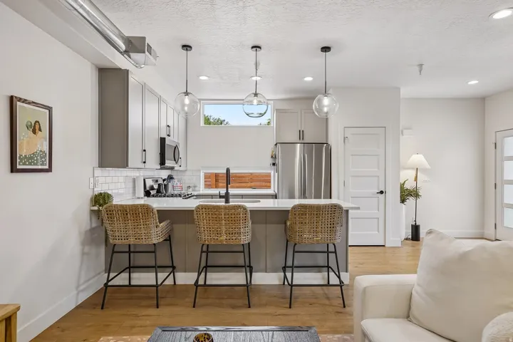 Modern kitchen featuring a breakfast bar with pendant lighting, stainless steel appliances, light gray cabinetry, and a white subway tile backsplash