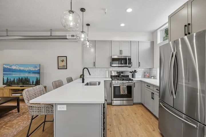 Modern kitchen featuring light gray cabinetry, stainless steel appliances, white subway tile backsplash, a large kitchen island with a white countertop and undermount sink, and wood-finish flooring