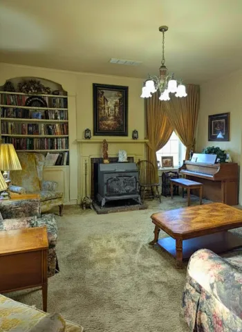 Living area with built-in arched shelving, an ornate chandelier, a traditional wood-burning stove on a brick hearth, and a window with drapery