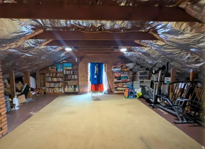 Expansive attic space featuring exposed wood beams, reflective insulation, and recessed lighting