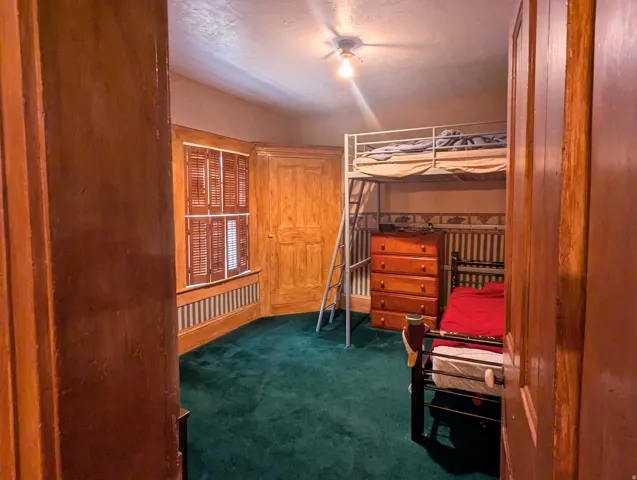 Interior room featuring deep green carpeting, wooden wall paneling, and a window with plantation shutters