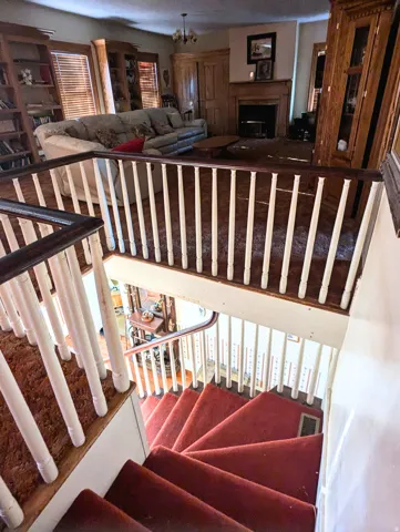 Staircase with red carpeted treads and white balusters, featuring dark wood handrails