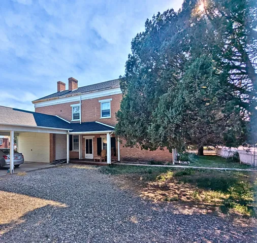 Brick exterior home featuring a covered porch, a carport, and twin chimneys